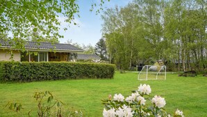 Een huis met een verzorgd gazon, een voetbalkooi en een haag ervoor.