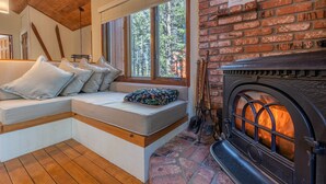 Quarto aconchegante com um banco embutido, lareira e uma grande janela com vista para uma floresta.
