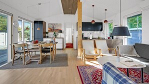 Amplia sala de estar con mesa de comedor, sillas, sofá y cocina equipada con televisor y electrodomésticos modernos.