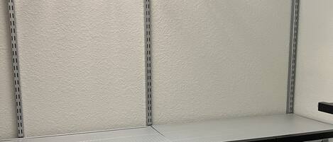 A storage closet with metal shelves, a metal rack, and a white textured wall.