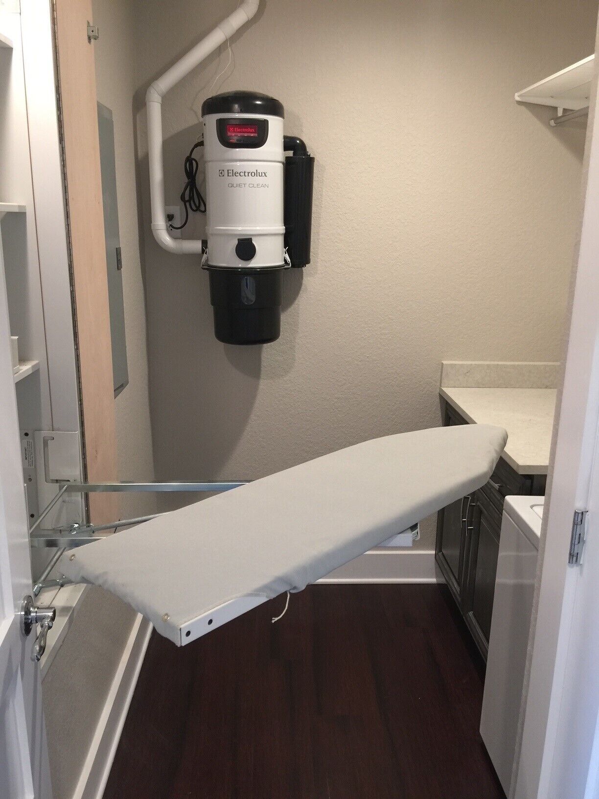A medical examination room with a white examination table, a wall-mounted Electrolux Quiet Clean vacuum cleaner, and a wooden floor.
