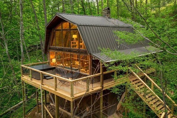Une cabane en bois dotée d’une façade en verre, d’une terrasse et d’un escalier.