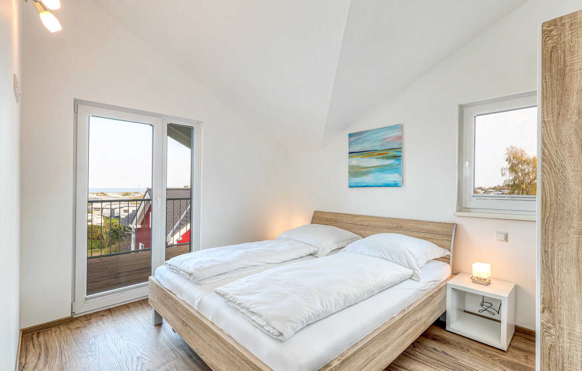A bedroom with a bed, a nightstand, a painting, and a window with a view.