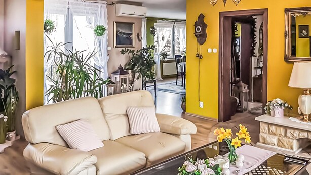 A living room with a beige sofa, yellow walls, and a chandelier. There are plants, a dining area, and a mirror in the background. - Gorgeous home in Raciaz with WiFi (Raciaz)