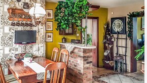 A cozy dining area with a brick fireplace, a wooden dining table with chairs, a television mounted on the wall, and various decorative items including a clock and plants. - Gorgeous home in Raciaz with WiFi (Raciaz)
