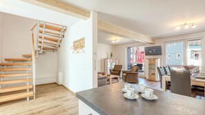 A modern kitchen with a central island, wooden staircase, and a dining area with chairs and a table. - Beach front home in Süssau/Ostsee with sauna (Süssau/Ostsee)