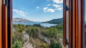 Blick von einem Zimmer mit Holztür auf eine gebirgige Landschaft mit See und klarem Himmel.