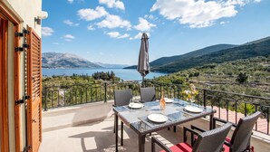 Eine Terrasse mit Esstisch, mit Blick auf einen See und Berge.
