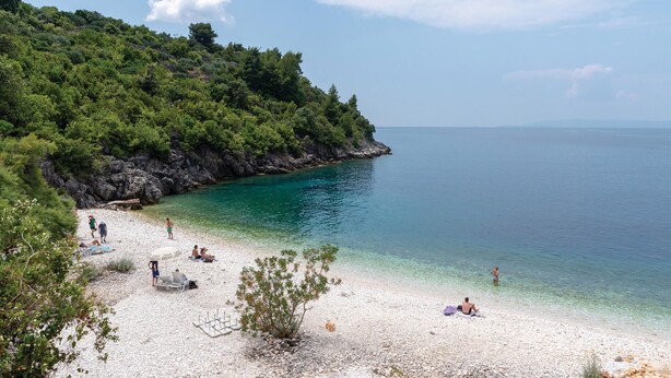 Ein Strand mit klarem türkisblauem Wasser, weißem Sand und felsigen Klippen.