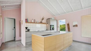 Une cuisine moderne dotée d’un îlot central, de meubles blancs et offrant une vue sur la verdure environnante.