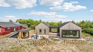 Une maison de plage moderne dotée d’une grande baie vitrée, d’une terrasse en bois et d’un petit jacuzzi.