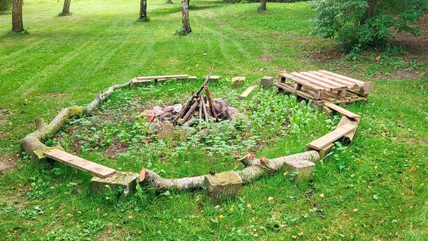 Pyöreä nuotiopaikka, jonka ympärillä on kivestä ja puusta rakennettu aita, sijaitsee vehreällä puistoalueella.
