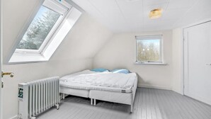 Pieni, valkoinen makuuhuone, jossa on kalteva katto, yksi sänky, patteri ja kaksi ikkunaa.