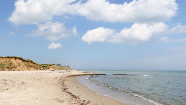 Ein Strand mit sandigem Ufer, einer grasbewachsenen Klippe und einem ruhigen Meer unter blauem Himmel.
