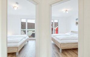 A modern bedroom with two beds, wooden flooring, and large windows offering views of neighboring buildings. - Beach front home in Süssau/Ostsee with sauna (Süssau/Ostsee)