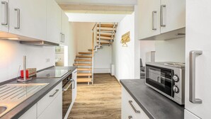 Eine moderne Küche mit einer Holztreppe, Edelstahlgeräten und weißen Schränken.