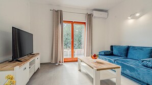 Una sala de estar moderna con un televisor sobre un mueble de madera, un sofá azul, una mesa de centro de madera y un ventanal corredero que da a un espacio exterior.