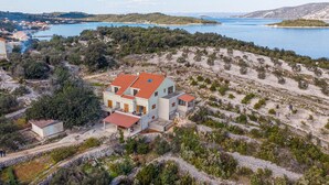 Propiedad costera con una casa grande de techo de tejas rojas, rodeada de olivares y una vista panorámica del mar.