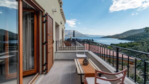 Un balcón con vistas a un lago y montañas, muebles de madera y barandilla.