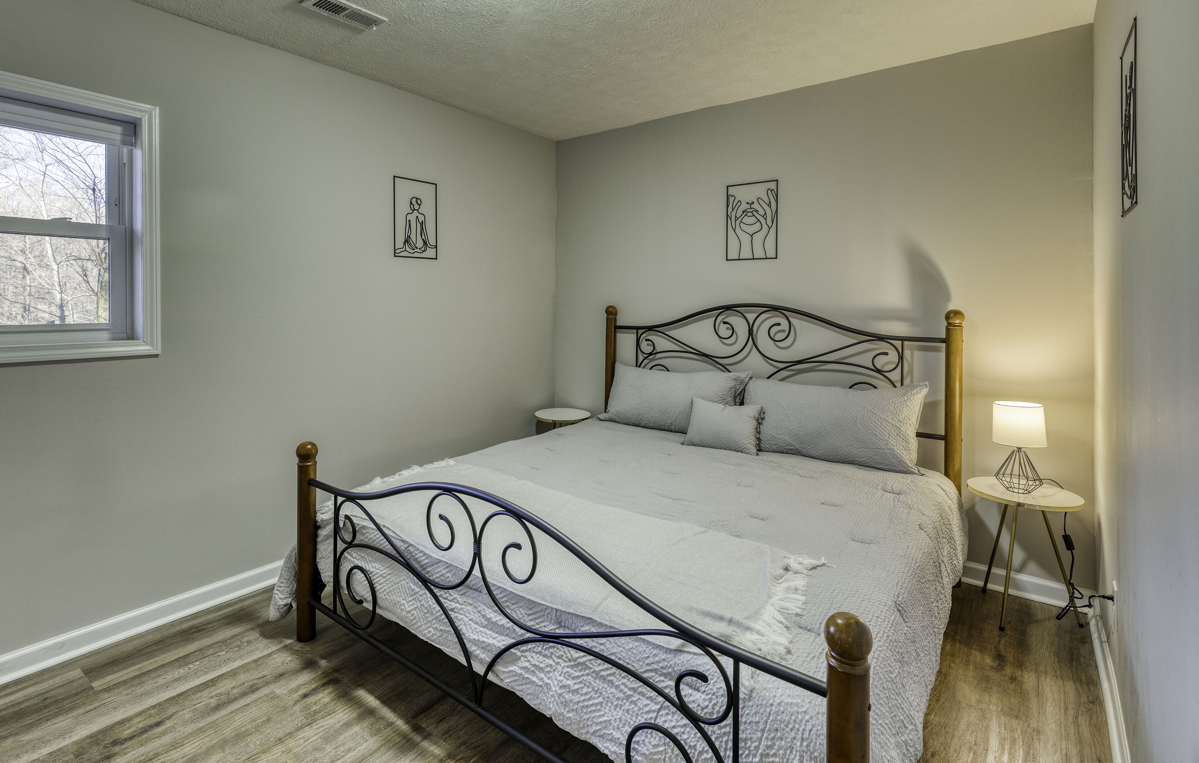Une chambre à coucher avec un lit en métal, une table de chevet avec une lampe et deux tableaux accrochés au mur.