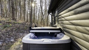 A hot tub with a stone exterior, positioned outdoors next to a wooden cabin. - Lake, Fun, BBQ & Family. Charming & Cozy HOME! (morganton)