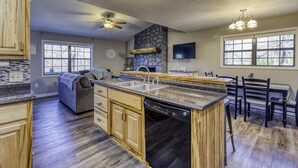 A kitchen with wooden cabinets, a stone accent wall, a built-in dishwasher, and a dining area with a table and chairs. - Lake, Fun, BBQ & Family. Charming & Cozy HOME! (morganton)