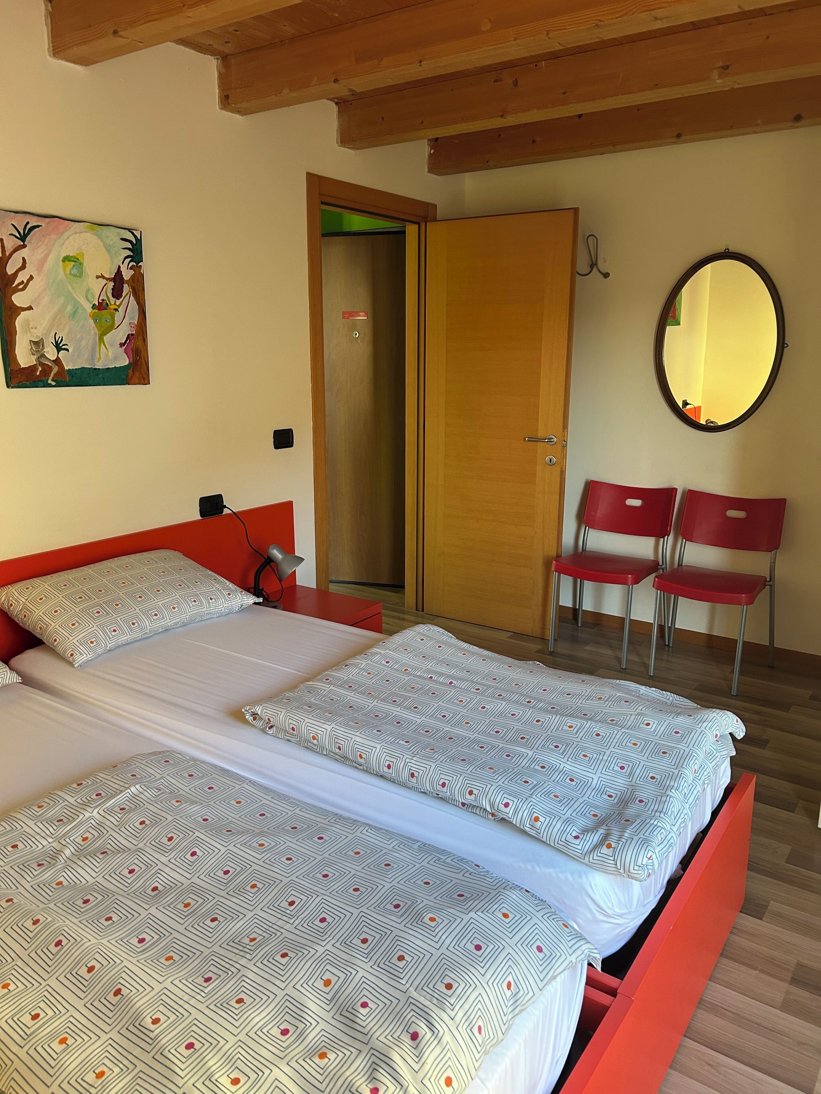 Une chambre avec deux lits, un plafond en bois, une porte, un miroir et une chaise rouge.