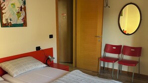 Ein Schlafzimmer mit zwei Betten, einer Holzbalkendecke, einer Tür, einem Spiegel und einem roten Sessel.