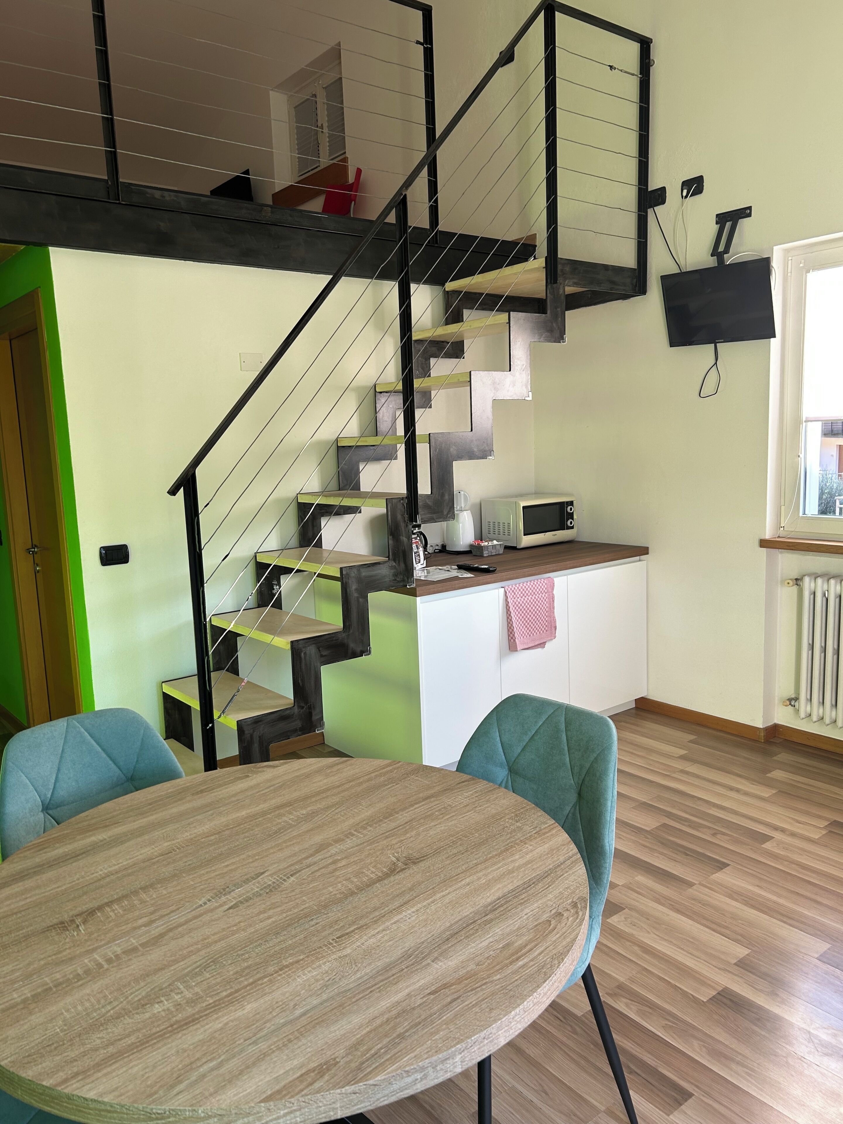 Eine moderne Küche mit Mikrowelle, Wasserkocher und weiteren Geräten auf der Arbeitsfläche. Eine Treppe mit schwarzer Geländer führt in einen oberen Bereich.