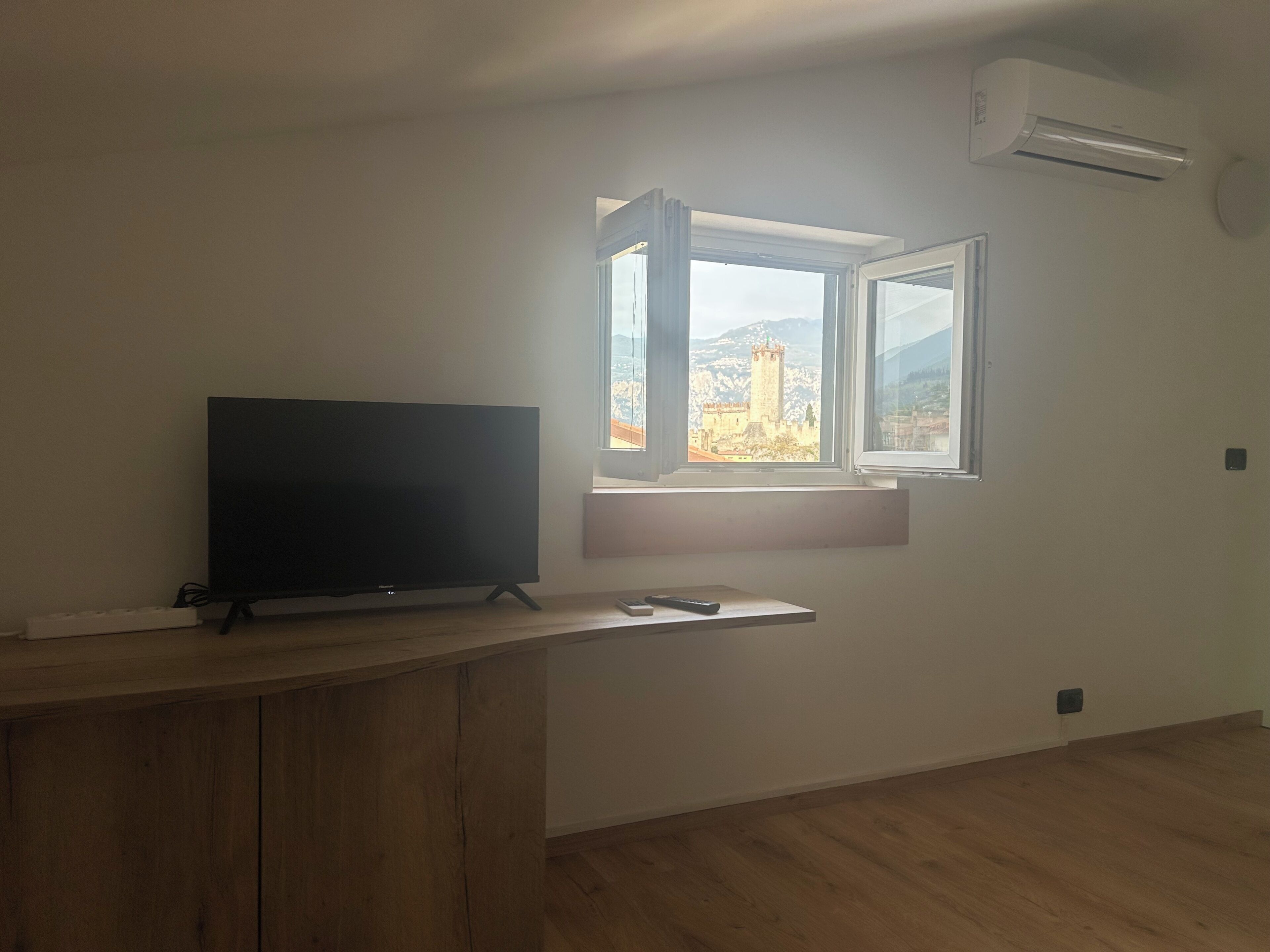 Ein Zimmer mit Fernseher auf einem Holztisch, einem Fenster mit Blick auf ein Schloss und einer Wandklimaanlage.