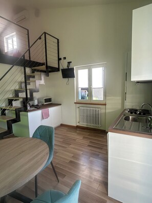 Eine Küche mit Treppe, einem Essbereich mit Stühlen, einem Heizkörper und einem Fenster.