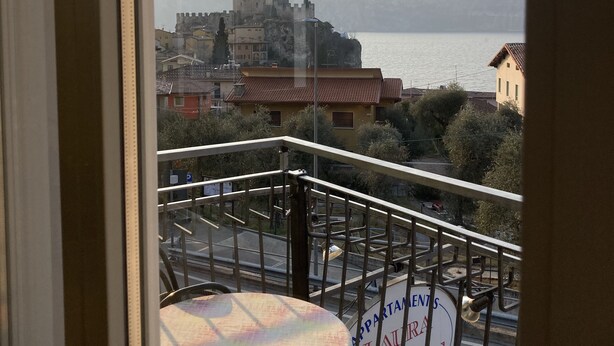 Ein Balkon mit Tisch und Stühlen, der auf eine Stadt mit einer festungsähnlichen Struktur und Berge in der Ferne blickt.