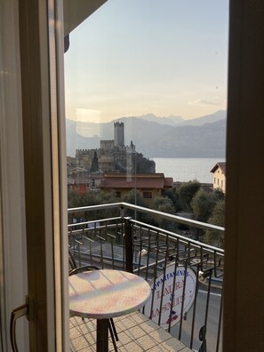 Un balcone con tavolo e sedie, affaccia su una città con una struttura simile a un castello e montagne sullo sfondo.