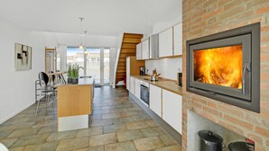 A modern kitchen with a fireplace, a dining area with a view, and a staircase leading to an upper level. - 2 bedroom cozy home in Rømø (Rømø)