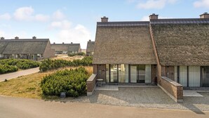 A row of modern buildings with thatched roofs, surrounded by a gravel driveway and greenery. - 2 bedroom cozy home in Rømø (Rømø)