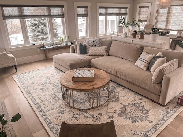 Un salon chaleureux avec un canapé d’angle beige, une table basse ronde et un tapis à motifs.
