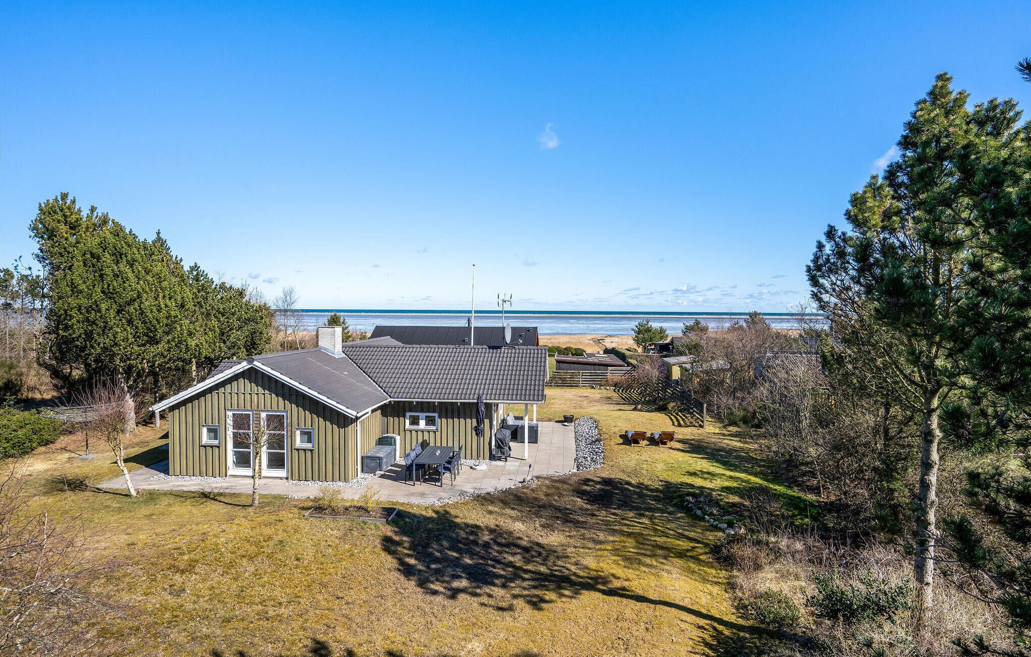 Ein eingeschossiges Haus mit Terrasse und Blick auf den Strand, bewölkter Himmel.
