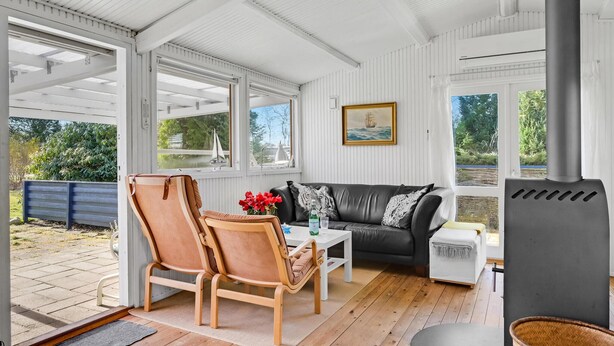 Une pièce chaleureuse et bien éclairée, avec un plancher en bois, un canapé en cuir, deux chaises en bois, une petite table blanche et un radiateur gris.
