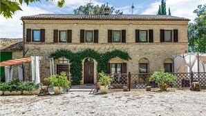 Un bâtiment en pierre de deux étages, doté d’un toit en tuiles, de fenêtres en arc de cercle et d’un espace extérieur aménagé avec des plantes, où l’on peut s’asseoir à l’abri.