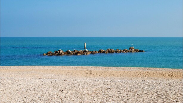 Une plage de galets avec un affleurement rocheux dans la mer.