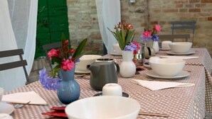 Une table à manger dressée avec des bols, des assiettes et des couverts blancs, agrémentée de vases de fleurs et d’une théière.