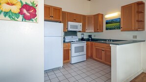 A kitchen with wooden cabinets, a white refrigerator, a microwave, a stove, and a sink. - 180' view 🌊& Mountain View! 1000 feet to 🏝watch 🌅 (Koloa)