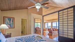 A bedroom with a large bed, a ceiling fan, and a view of a balcony with wicker furniture. - 180' view 🌊& Mountain View! 1000 feet to 🏝watch 🌅 (Koloa)