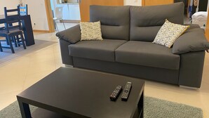 Ein modernes Wohnzimmer mit einem grauen Sofa, zwei gemusterten Zierkissen, einem schwarzen Couchtisch und zwei Fernbedienungen.