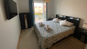 Ein Hotelzimmer mit Bett, Fernseher, Fenster mit Vorhängen, Deckenventilator und Klimaanlage.