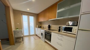 Eine moderne Küche mit Waschmaschine, Backofen, Mikrowelle und einem großen Fenster mit Jalousien.