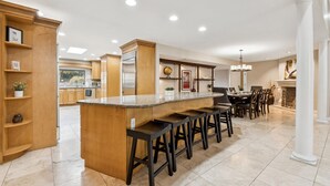 A modern kitchen with a central island, bar stools, wooden cabinetry, and a dining area with a chandelier. - The Big Dog – Private Custom Estate – Heated Pool & Spa – Game Room (SCOTTSDALE)