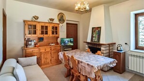 A cozy kitchen with wooden cabinets, a dining table with a patterned tablecloth, a fireplace, and a television. - 2 bedroom awesome home in Preci (Preci)