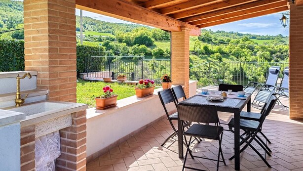 A covered patio with a table and chairs, a brick wall, and a view of a green landscape. - 2 bedroom awesome home in Preci (Preci)