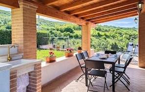 Un portico coperto con tavolo e sedie, un muro in mattoni e vista su un paesaggio verde.